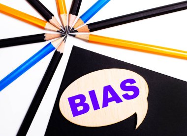 Çok renkli kalemlerin yanında siyah bir zemin üzerinde BIAS yazılı tahta kart..