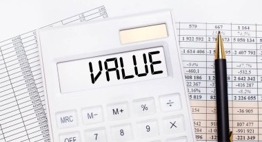 Masaüstünde raporlar var, skorbordunda VALUE yazılı beyaz bir hesap makinesi ve bir kalem. İş konsepti.