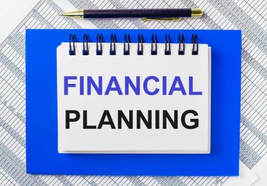 Masaüstündeki raporların arka planında mavi bir not defteri var. FINANCIAL PLANNING 'in yazılı olduğu bir kalem ve beyaz bir defter var. İş konsepti