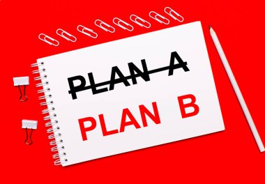 Parlak kırmızı bir arka planda, beyaz bir kalem, beyaz ataçlar, ve beyaz bir defter üzerinde