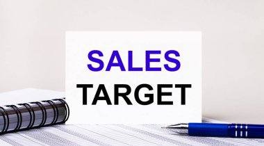 Açık gri bir arka planda, bir defter, mavi bir kalem ve içinde SALES TARget yazan bir kağıt. İş konsepti