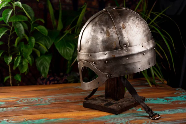 Gjermundbu viking helmet stands on a wooden table and against the background of plants