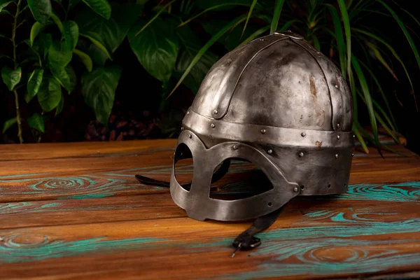 Gjermundbu viking helmet stands on a wooden table and against the background of plants