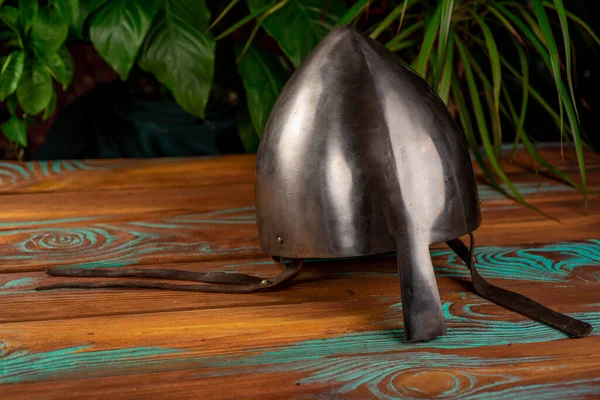 Ahşap arka planda bitkilerle burun koruması olan eski metal rekonstrüksiyon miğferi