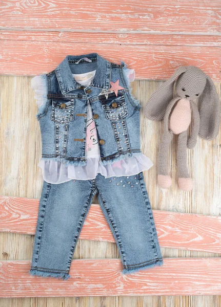 Tişörtlü kot pantolon ve pantolon ile ahşap bir masada tavşan oyuncağı.