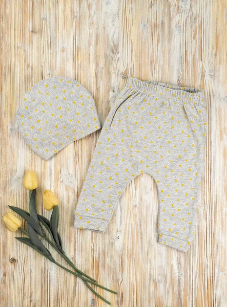 Çiçekteki pantolonu boyayan gri şapka. Tahta bir masada lalelerle yatan bebek.