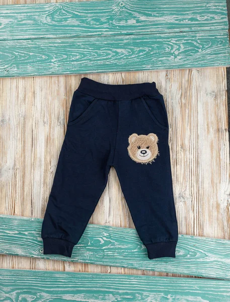 Dark blue pants with a drawing of a bear for a kid lie on a wooden table