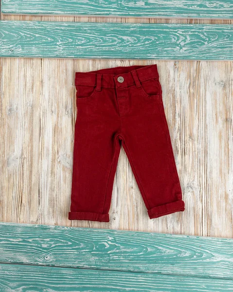 Little red jeans for  baby lying on wooden background
