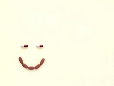 Bej bir arka planda gülümseme şeklinde haplar ve kapsüller.