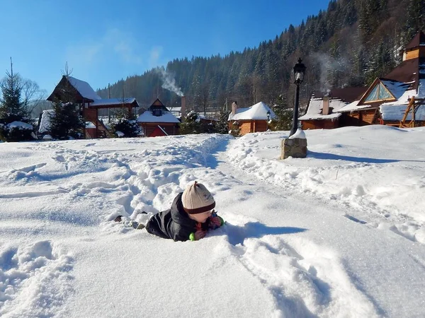 Kleiner Junge Liegt Schnee Inmitten Eines Bergdorfes Mit Holzhäusern — Stockfoto