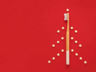 Bambu diş fırçası ve tabletlerdeki eko diş macunu. Kırmızı arka planda yaratıcı bir Noel ağacı. Plastiksiz, sıfır atık.