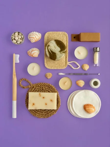 Eco hygiene products: bamboo toothbrush, toothpaste in tablets, dental floss, cotton sponge, natural washcloth, homemade soap. High angle view on violet background. Creative geometry.