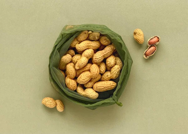 Peanuts in shell and reusable mesh bag on green paper background, natural zero waste concept
