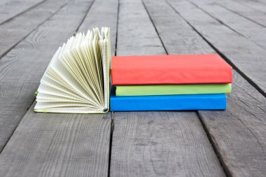 Stack of books and open book with fanned pages on wooden floor a