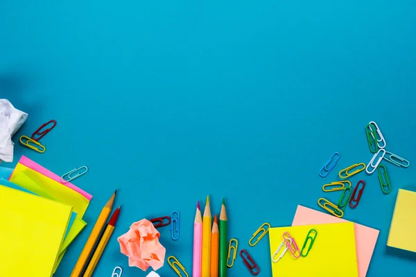 Escritorio de mesa de oficina con conjunto de suministros de colores, bloc de notas blanco, taza, pluma, PC, papel arrugado, flor sobre fondo azul. Vista superior y espacio de copia para texto — Foto de Stock