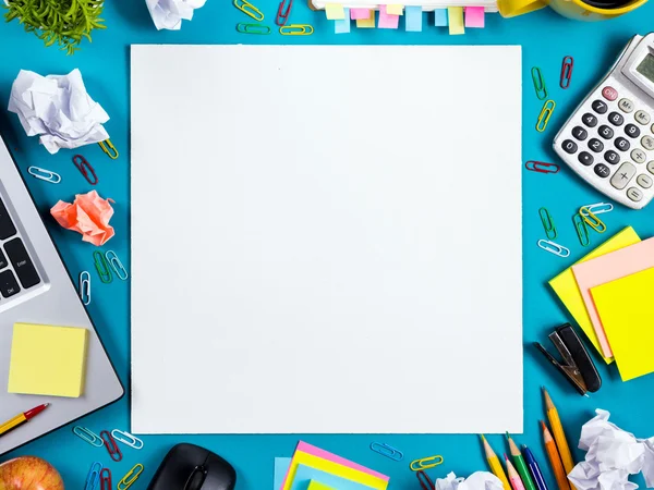 Τραπέζι γραφείο με σύνολο πολύχρωμο προμήθειες, λευκό κενό σημειωματάριο, Κύπελλο, στυλό, pc, τσαλακωμένο χαρτί, λουλούδια σε μπλε φόντο. Κορυφαία άποψη και αντίγραφο χώρο για κείμενο — Φωτογραφία Αρχείου