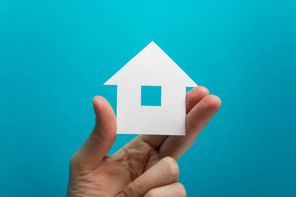 Hand holding white paper house figure on blue background. Real Estate Concept. Ecological building. Copy space top view. — Stock Fotó