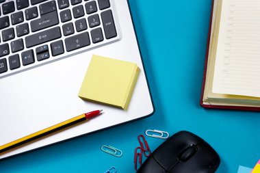 Ofis tablo Masası dizi renkli malzemeleri, beyaz boş not defteri, Kupası, kalem, pc, buruşuk kağıt, ile mavi arka plan üzerinde çiçek. Metin için en iyi görünüm ve kopya yer