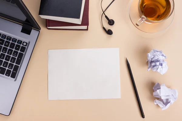 Office table desk with set of colorful supplies, white blank note pad, cup, pen, pc, crumpled paper, flower on beige background. Top view and copy space for text — Stock Photo, Image