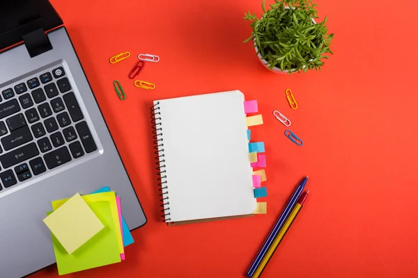 Schreibtisch mit buntem Zubehör, weißem Notizblock, Tasse, Stift, PC, zerknülltem Papier, Blume auf rotem Hintergrund. Ansicht von oben und Kopierraum für Text — Stockfoto