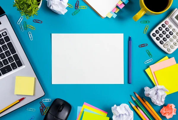 Schreibtisch mit buntem Zubehör, weißem Notizblock, Tasse, Stift, PC, zerknülltem Papier, Blume auf blauem Hintergrund. Ansicht von oben und Kopierraum für Text — Stockfoto