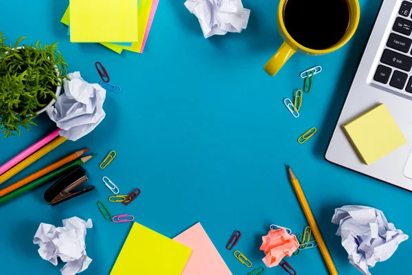 Schreibtisch mit buntem Zubehör, weißem Notizblock, Tasse, Stift, PC, zerknülltem Papier, Blume auf blauem Hintergrund. Ansicht von oben und Kopierraum für Text — Stockfoto