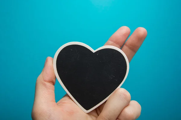 Love sign. Black board heart in woman hands on blue background — Stock Photo, Image