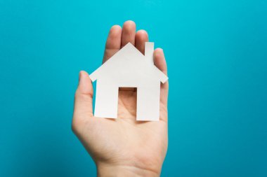 Hand holding white paper house figure on blue background. Real Estate Concept. Ecological building. Copy space top view.