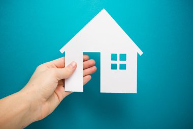 Hand holding white paper house figure on blue background. Real Estate Concept. Ecological building. Copy space top view.