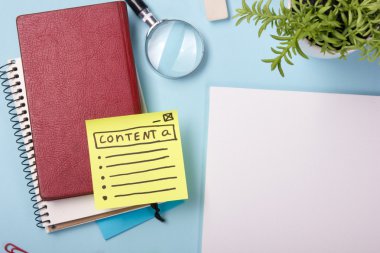 Ofis tablo büro malzemeleri, boş not defteri, Kupası, kalem, pc, buruşuk kağıt, ile mavi arka plan üzerinde çiçek. Üstten Görünüm