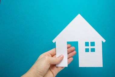 Hand holding white paper house figure on blue background. Real Estate Concept. Ecological building. Copy space top view.