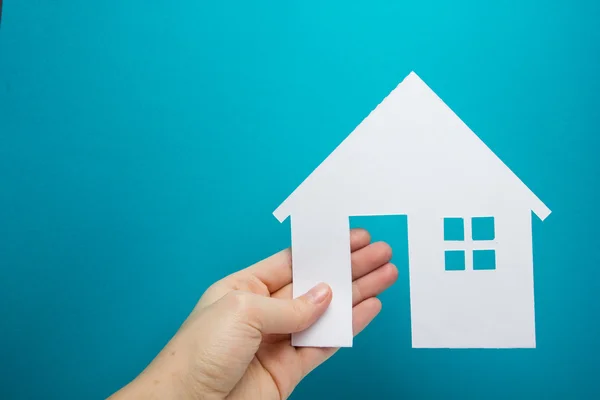 Mão segurando papel branco figura da casa no fundo azul. Conceito imobiliário. Edifício ecológico. Espaço de cópia vista superior . — Fotografia de Stock