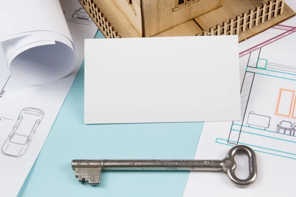 Concepto inmobiliario. Llave de plata con figura de la casa y tarjeta de visita en blanco sobre fondo azul. Vista superior . — Foto de Stock