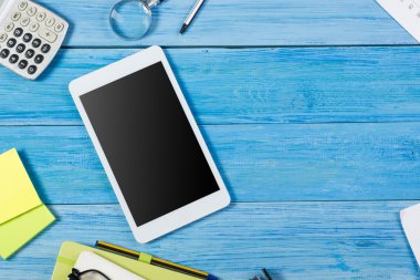 Tablet pc, renkli malzemeleri seti ile ofis masa masasında boş boş ekran, not defteri, fincan, kalem, çiçek mavisi arka plan. Reklam metni için en iyi görünüm ve kopyalama alanı