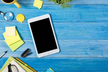 Tablet pc, renkli malzemeleri seti ile ofis masa masasında boş boş ekran, not defteri, fincan, kalem, çiçek mavisi arka plan. Reklam metni için en iyi görünüm ve kopyalama alanı