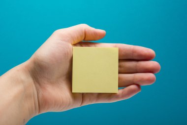 Yapışkan not, başparmak kadar parmak, mavi arka plan üzerinde sarı hatırlatma.