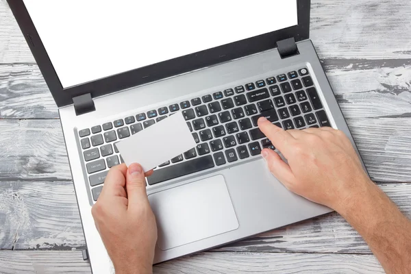 Hands holding business credit card typing numbers, laptop computer pc keyboard making online payment at home against grunge black and white wooden desk table On-line shopping concept Selective focus