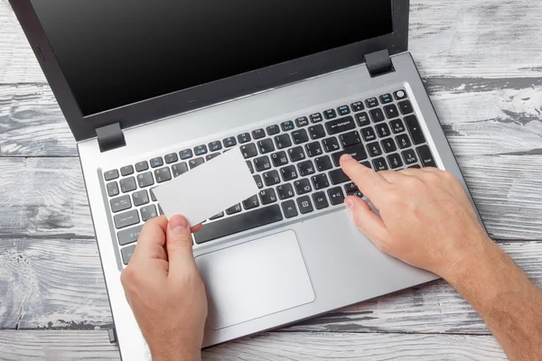 Hands holding business credit card typing numbers, laptop computer pc keyboard making online payment at home against grunge black and white wooden desk table On-line shopping concept Selective focus