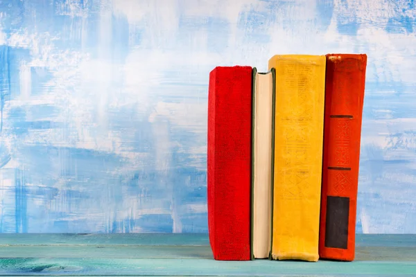 Σύνθεση με παλιά vintage πολύχρωμα βιβλία σκληρό πίσω στοίβαγμα, ημερολόγιο σε ξύλινο τραπέζι καταστρώματος και καλλιτεχνικό μπλε φόντο. Πίσω στο σχολείο. Αντιγραφή χώρου. Έννοια της εκπαίδευσης. — Φωτογραφία Αρχείου