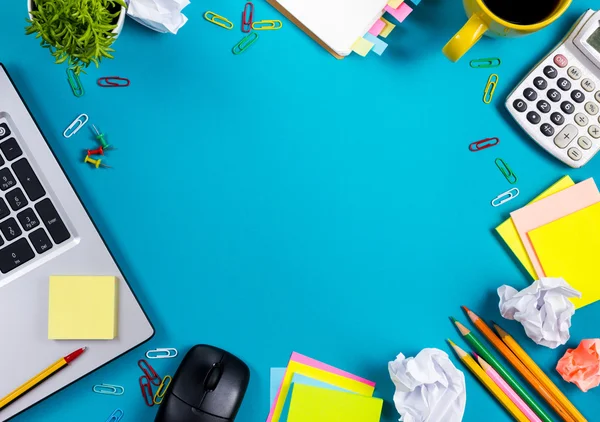 Schreibtisch mit buntem Zubehör, weißem Notizblock, Tasse, Stift, PC, zerknülltem Papier, Blume auf blauem Hintergrund. Ansicht von oben und Kopierraum für Text — Stockfoto