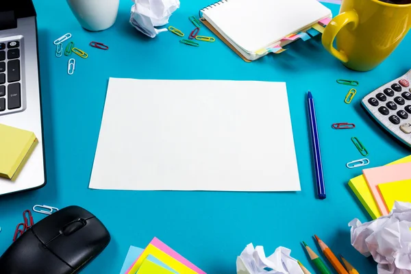 Schreibtisch mit buntem Zubehör, weißem Notizblock, Tasse, Stift, PC, zerknülltem Papier, Blume auf blauem Hintergrund. Ansicht von oben und Kopierraum für Text — Stockfoto