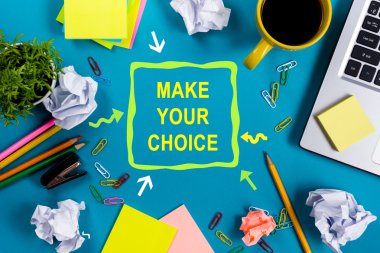 Seçimini yap. Malzemeleri ile Ofis masa masası, beyaz boş not defteri, fincan, kalem, pc, buruşuk kağıt, mavi arka plan üzerinde çiçek. Üstte görüntü