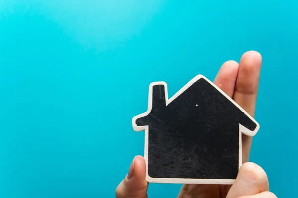 Рука держит фигурку белого бумажного дома на синем фоне. Концепция недвижимости. Копирование пространства сверху . — стоковое фото