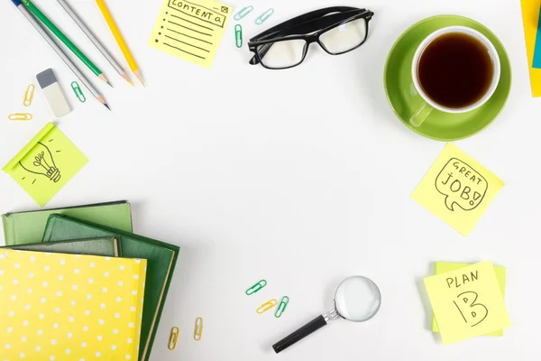 Mesa de escritório com suprimentos verdes, bloco de notas em branco, copo, caneta, óculos, papel amassado, lupa, flor sobre fundo branco. Vista superior — Fotografia de Stock