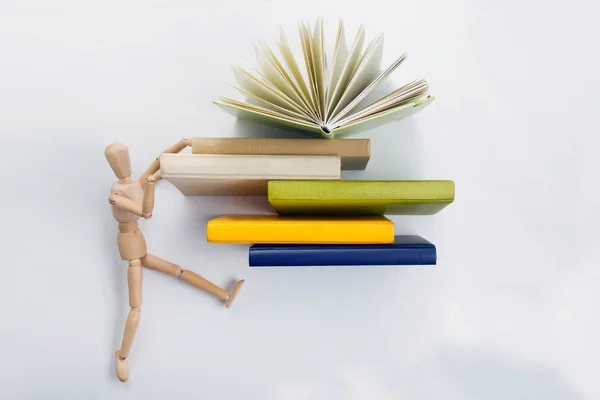 Wooden mannequin carries a stack of colorful books. — Stock Photo, Image