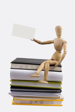 A stack of colorful books, open book. Wooden mannequin holding business card placard sitting on the stack of colorful books.