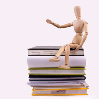 A stack of colorful books, open book. Wooden mannequin holding business card placard sitting on the stack of colorful books.