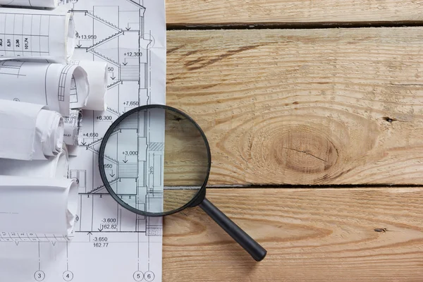 Architectural project, blueprints, blueprint rolls near checkered blank paper with pen on vintage wooden background. Construction concept. Architect workplace top view. Copy space — Stock Photo, Image