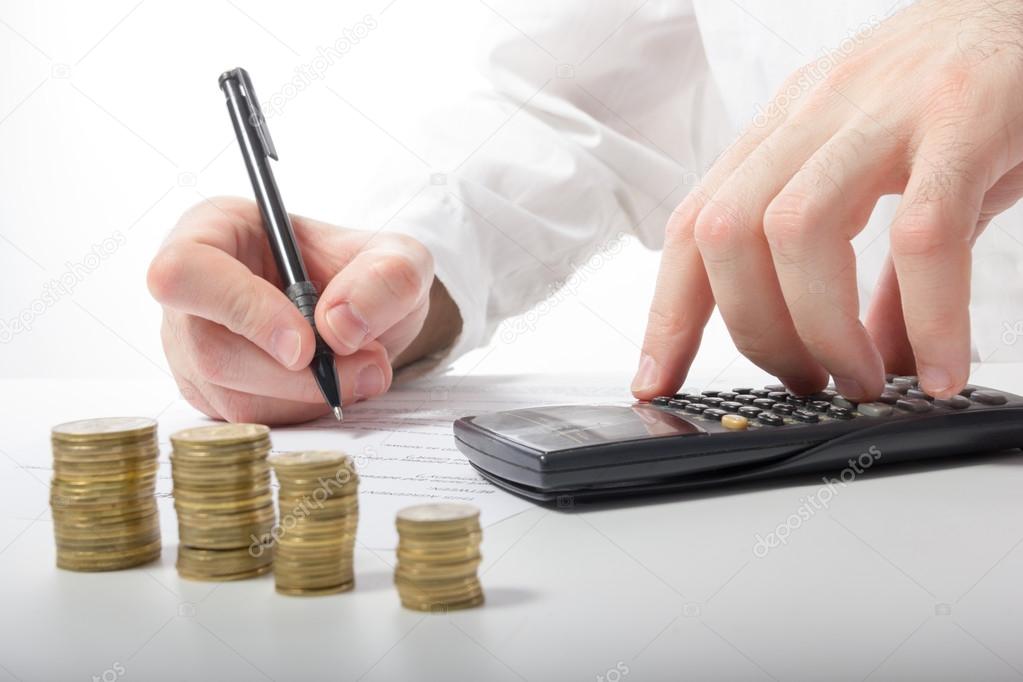 Business concept. Businessman's hand counting losses and profit working with statistics, analyzing financial results on calculator and signing documents at office workplace, office work. Stack of coins. Financial Accounting - money and calculator.