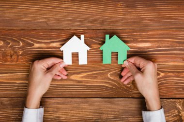 Hands holding green paper house figure models arrows on white background. Concept for comparision of real estate houses pricing Real Estate Concept. Top view, copy space. Eco house